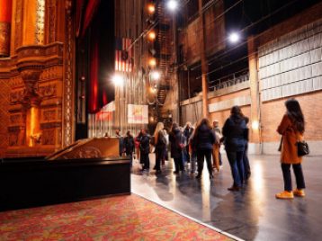 UM students group together on the stage of the Fox Theater as they listen to a guide